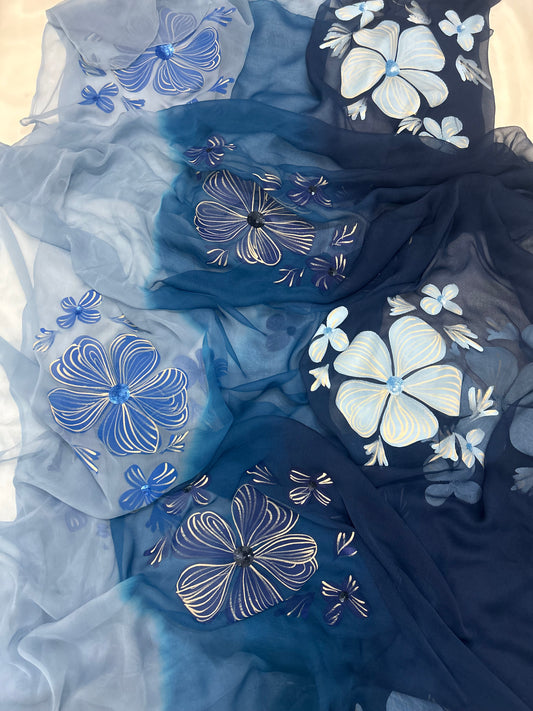 Hand-painted chiffon saree featuring a three-shade blue ombré gradient with large hand-painted light blue flowers and delicate sequin work highlights.